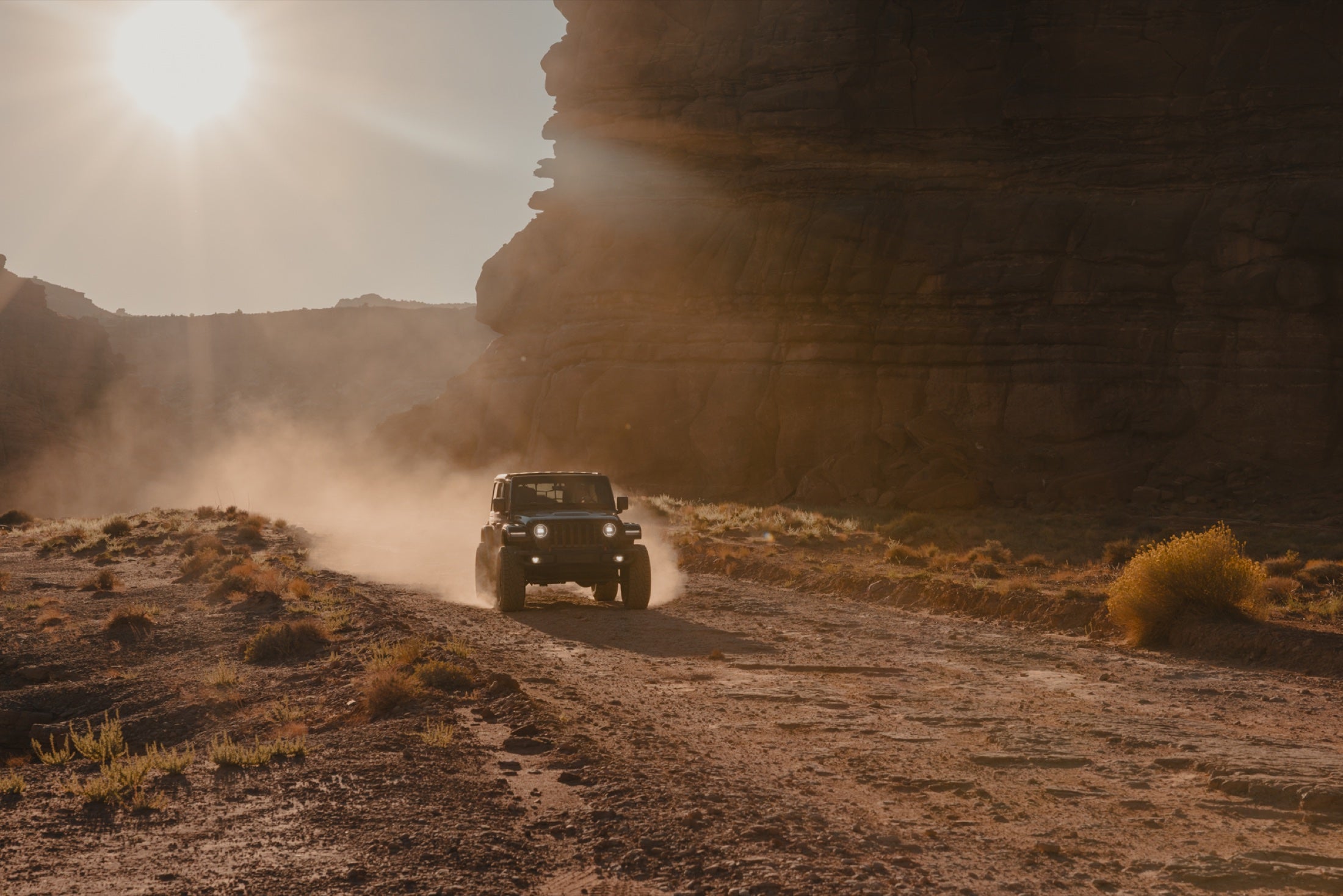 Jeep Wrangler driving through Moab dust at sunset